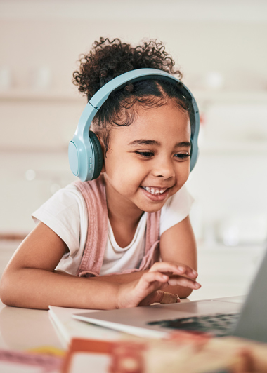 smiling girl wearing blue headphones using laptop at home enjoying sound and learning